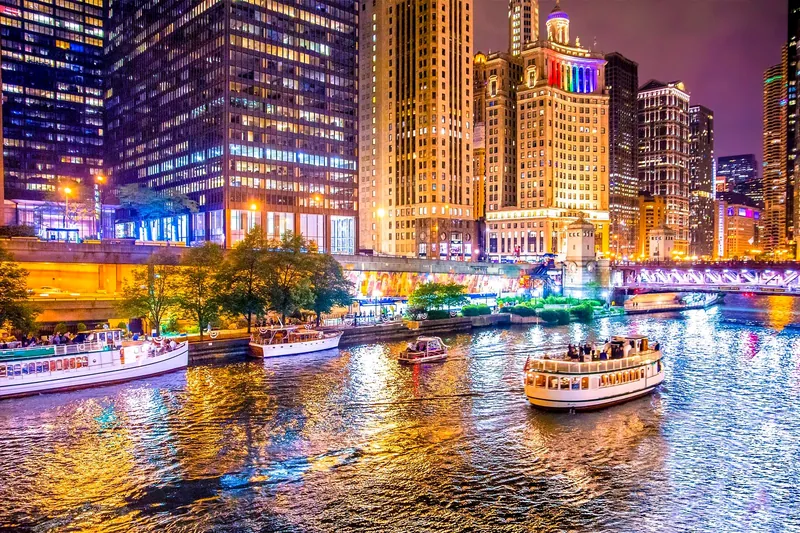 Chicago Riverwalk and tour boats lit up on a summer night